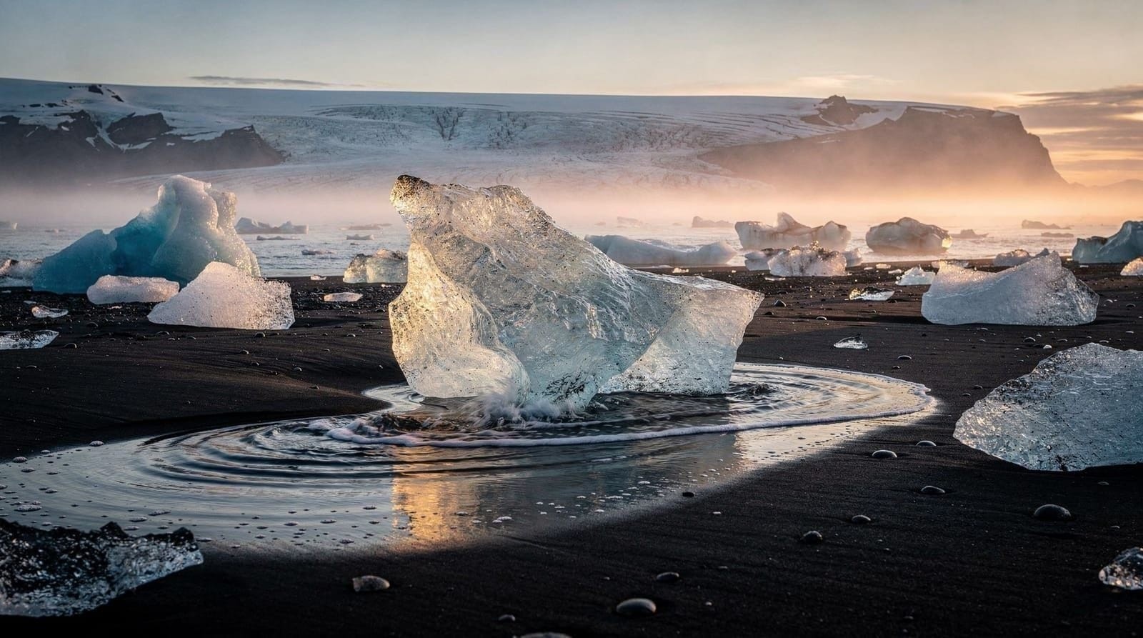 Glacier ice on a black sand beach at sunrise, with a glacier and mist behind